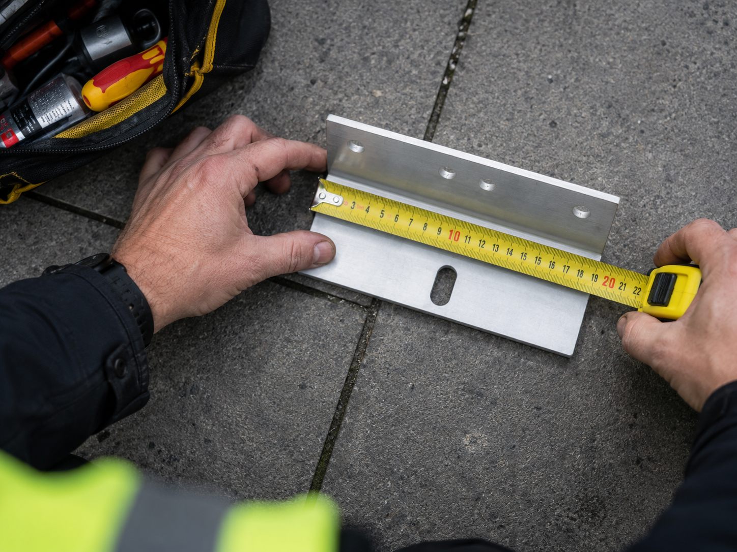 Hands measuring a mounting bracket with a tape measure on site